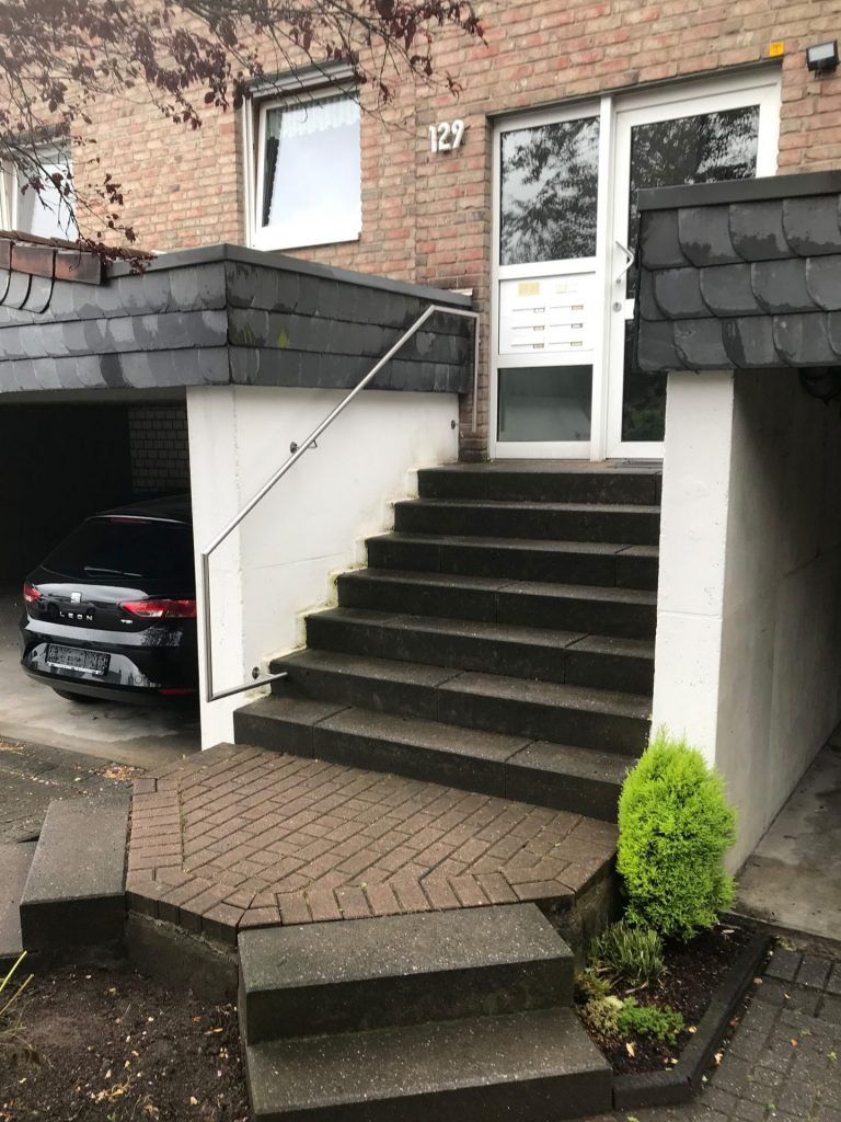 Mehrfamilienhaus-Eingang mit Treppenstufen und Edelstahl-Handlauf, sicher befestigt an Wand und Hauseingang.