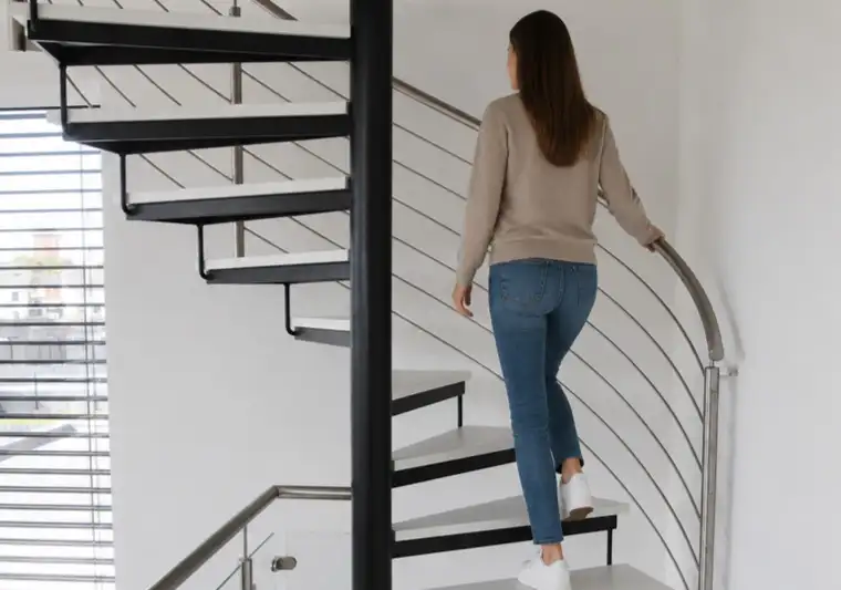 Eine Frau läuft eine Spindeltreppe von Janßen nach oben, mit weissen Stufen aus Holz und einem Edelstahlhandlauf