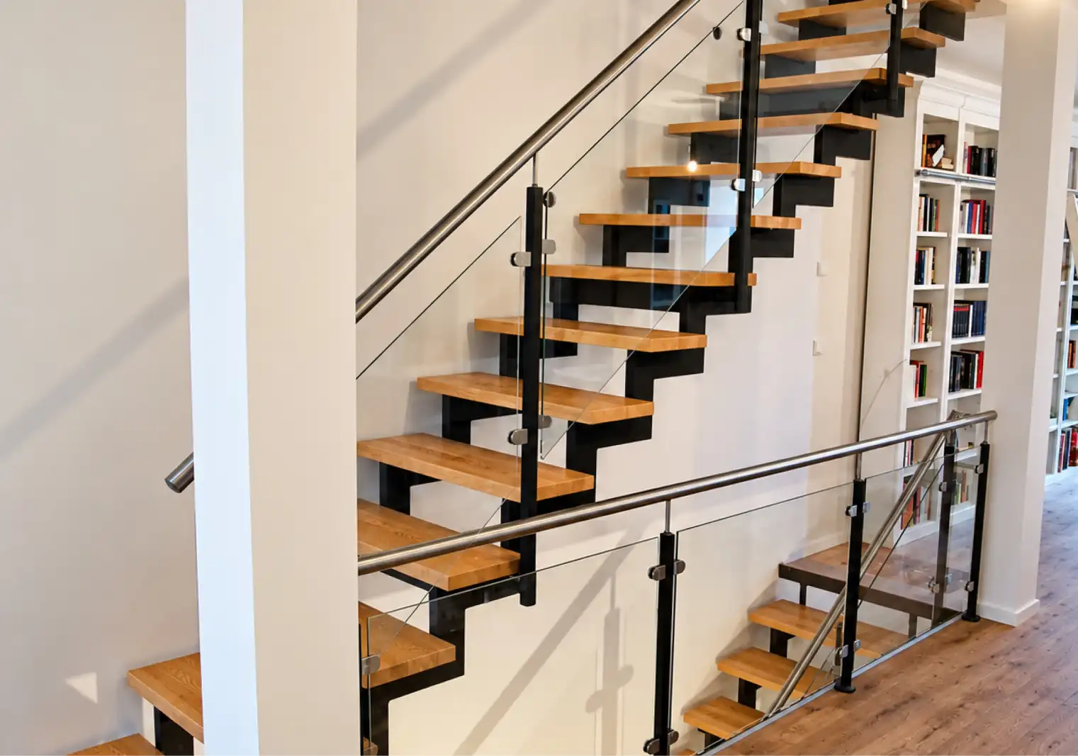 Zweiholmtreppe als Innentreppe mit Holzstufen aus Buche, Glasgeländer und Edelstahlhandlauf in einem Treppenhaus